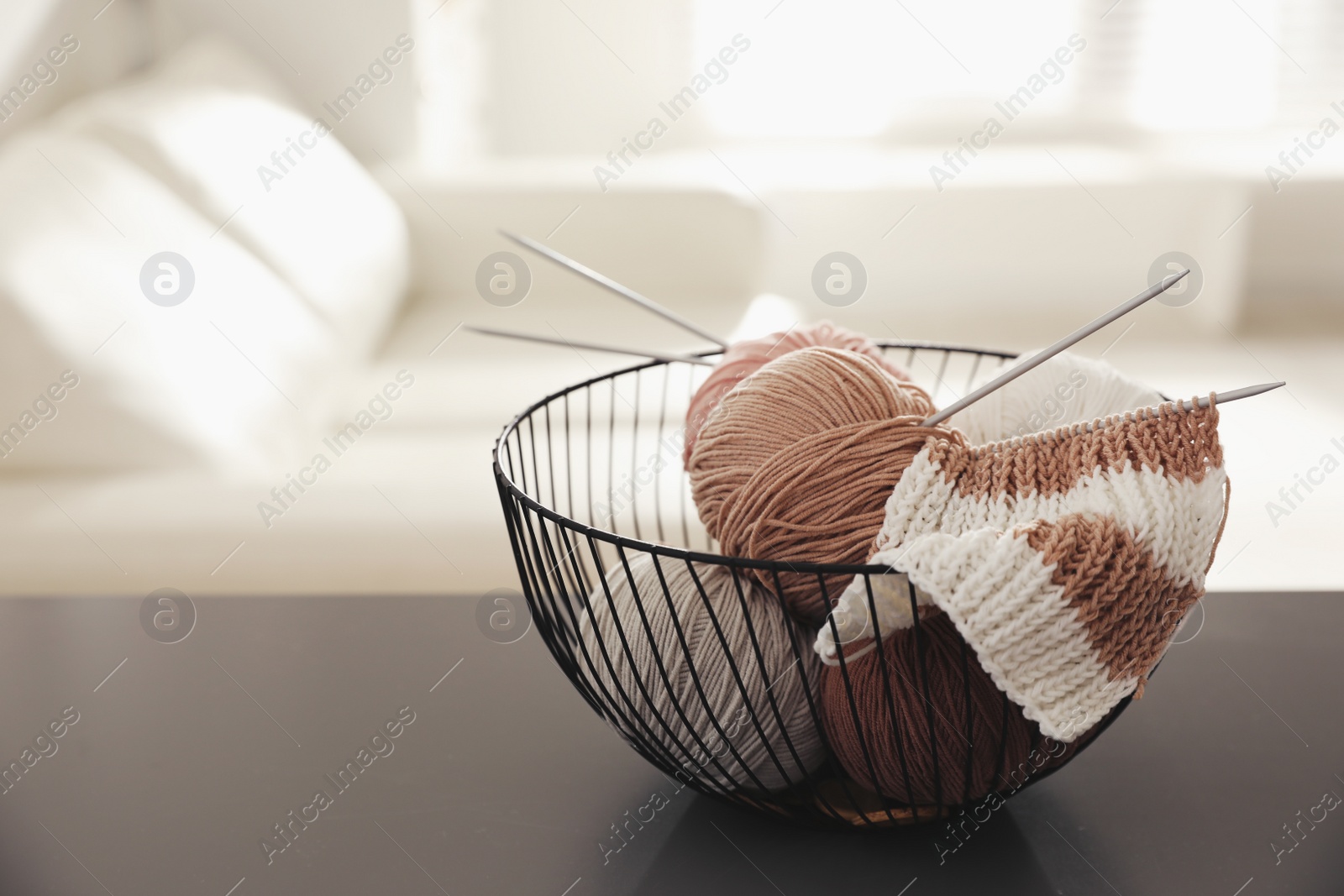 Photo of Yarn balls and knitting needles in metal basket on grey table indoors, space for text. Creative hobby