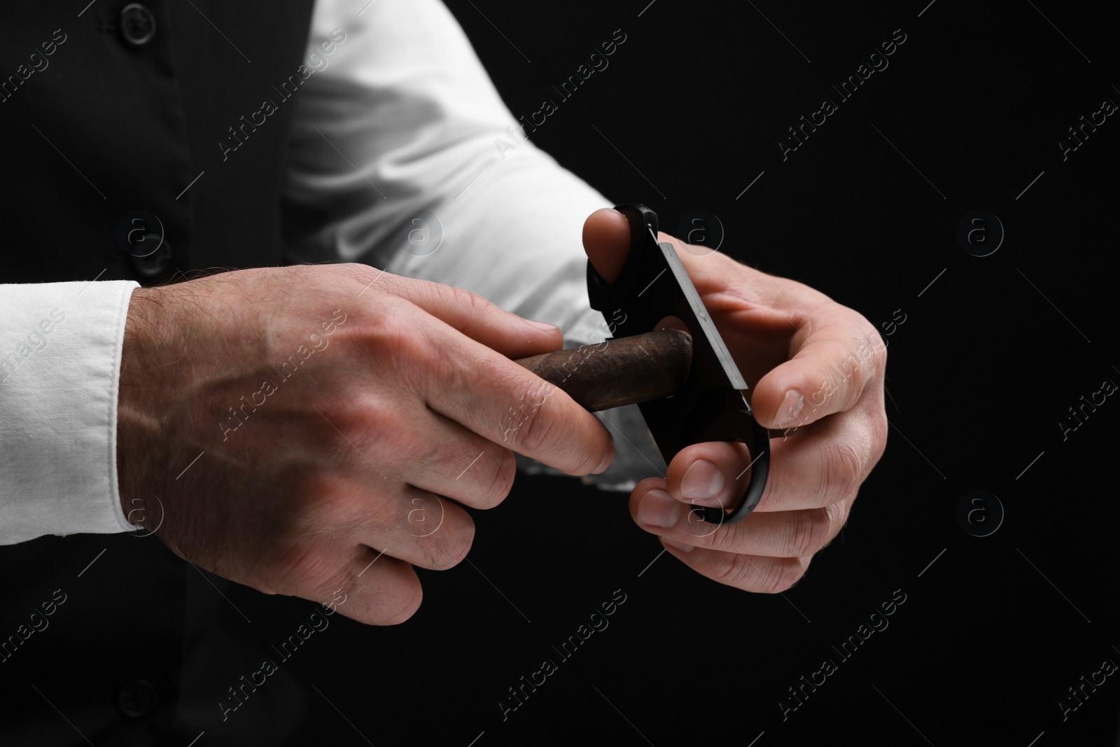 Photo of Man cutting tip of cigar on black background, closeup