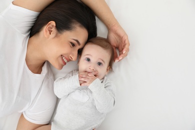 Portrait of mother with her cute baby lying on bed, top view. Space for text