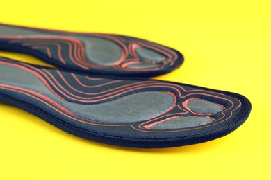 Pair of orthopedic insoles on yellow background, closeup