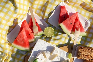 Photo of Delicious cheese, watermelon and bread on picnic blanket, flat lay