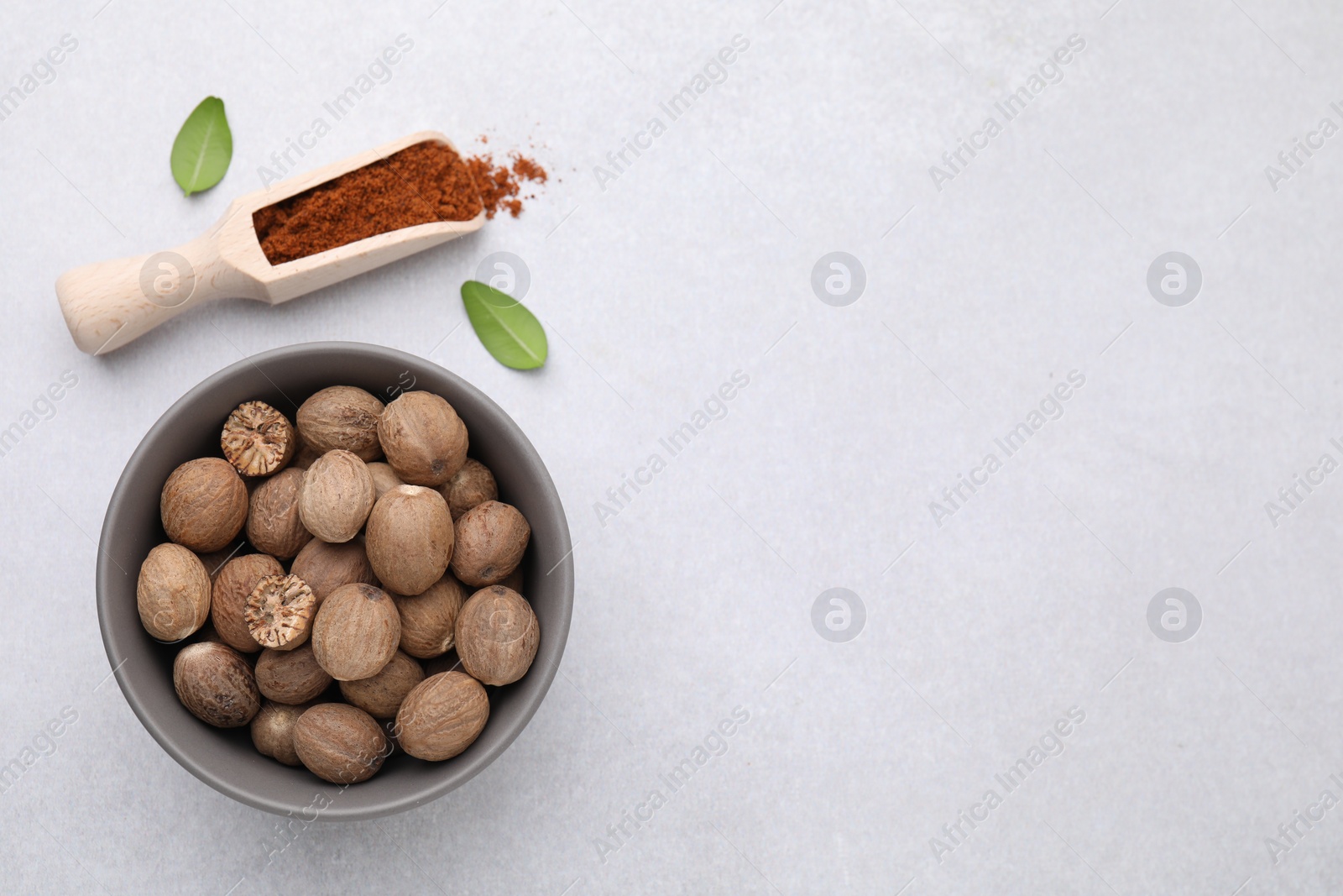 Photo of Scoop with nutmeg powder, seeds in bowl and green leaves on light table, flat lay. Space for text