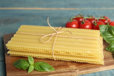 Photo of Uncooked lasagna sheets with basil and cherry tomatoes on wooden board, closeup