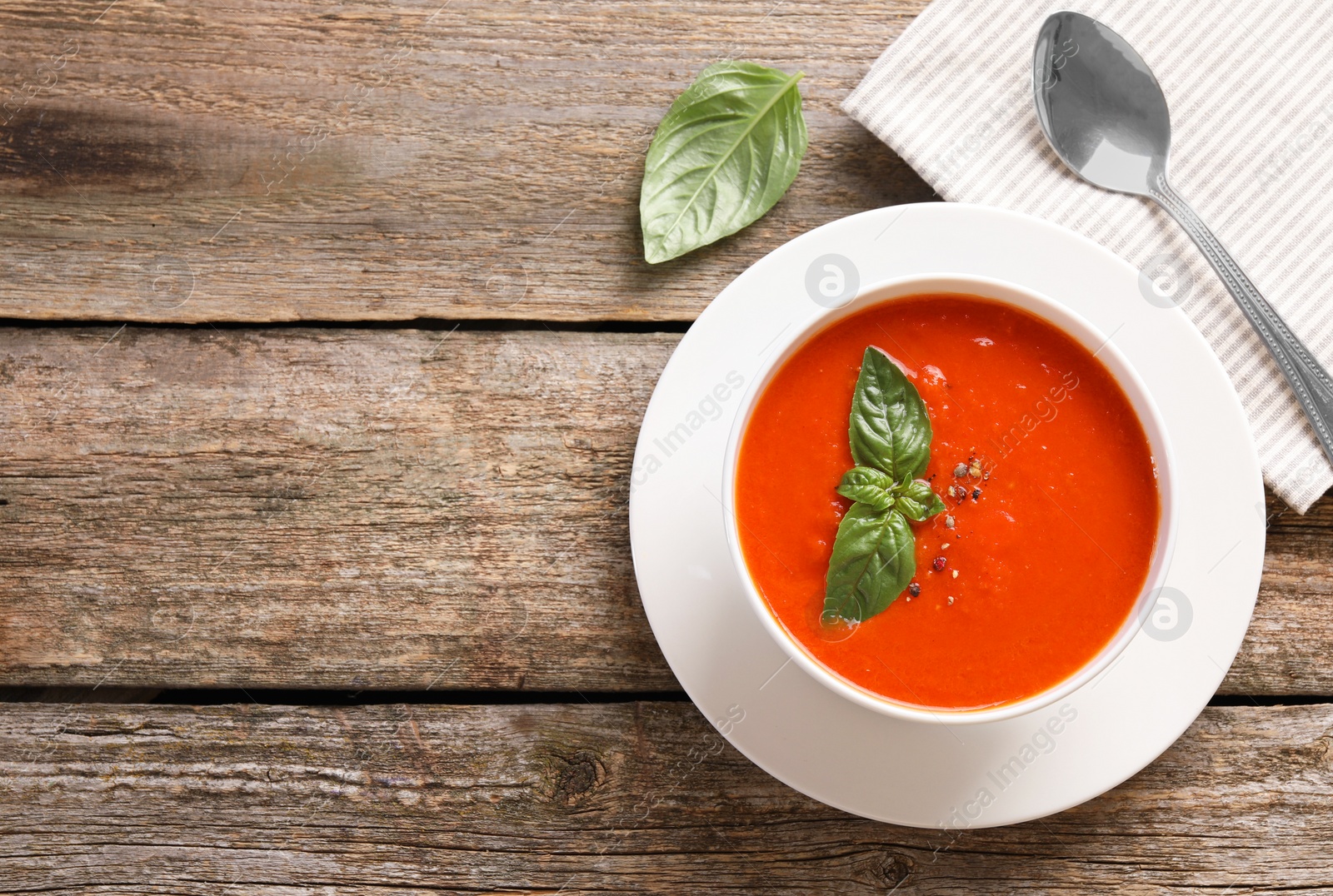 Photo of Delicious tomato soup with basil, spices and spoon on wooden table, flat lay. Space for text