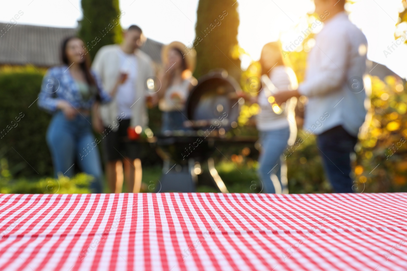 Photo of Empty table and blurred view of friends having barbecue party outdoors. Space for text