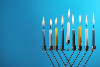Hanukkah celebration. Menorah with burning candles on light blue background, space for text