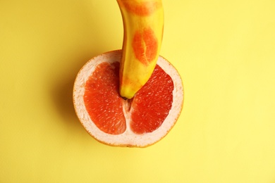 Photo of Fresh grapefruit and banana with red lipstick marks on yellow background, flat lay. Sex concept