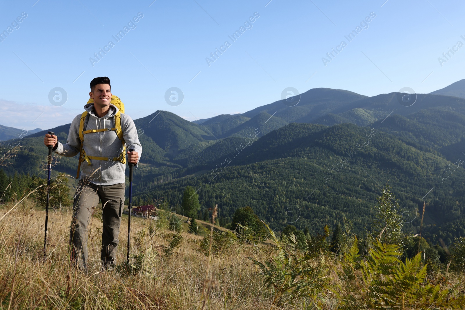 Photo of Tourist with backpack and trekking poles hiking through mountains, space for text