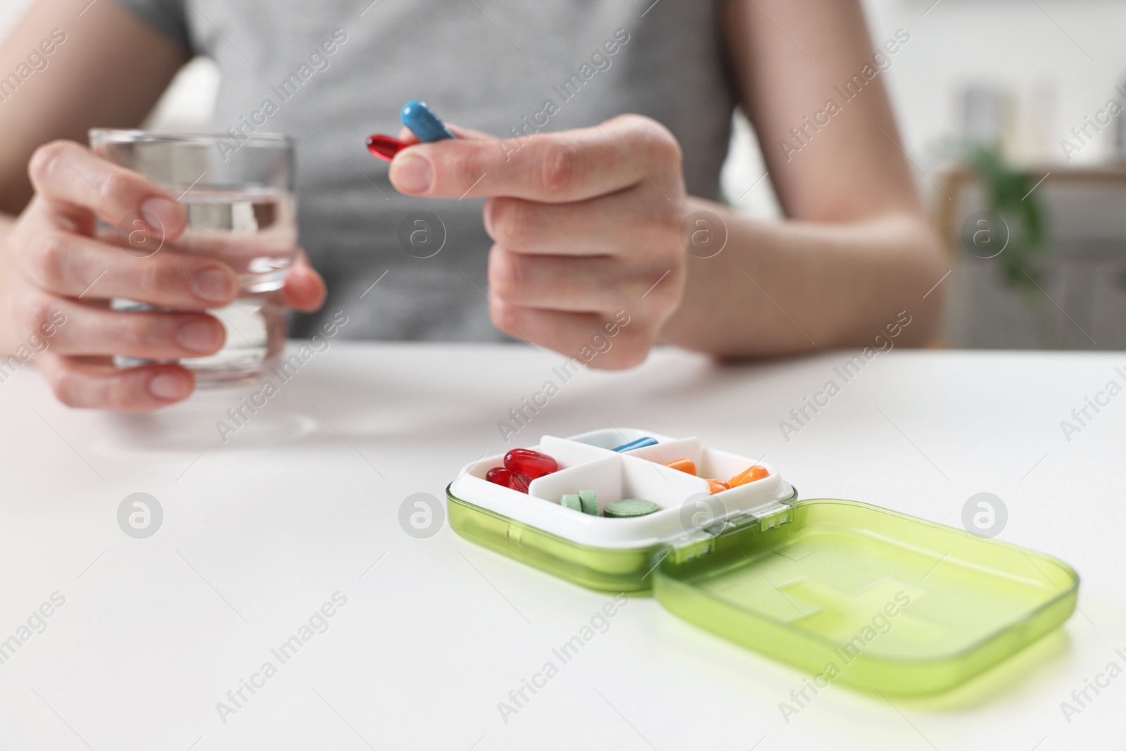 Photo of Woman with pills, organizer and glass of water at white table, closeup