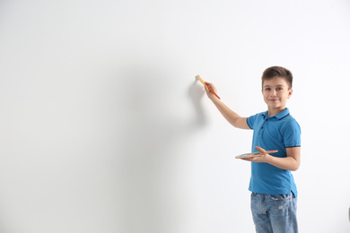 Photo of Little child painting on white wall indoors. Space for text