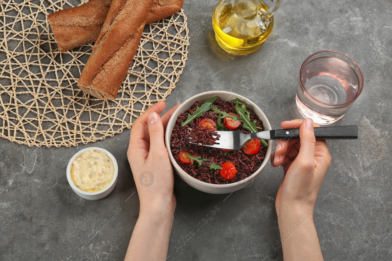 Photo of Woman eating tasty brown rice at grey table, top view