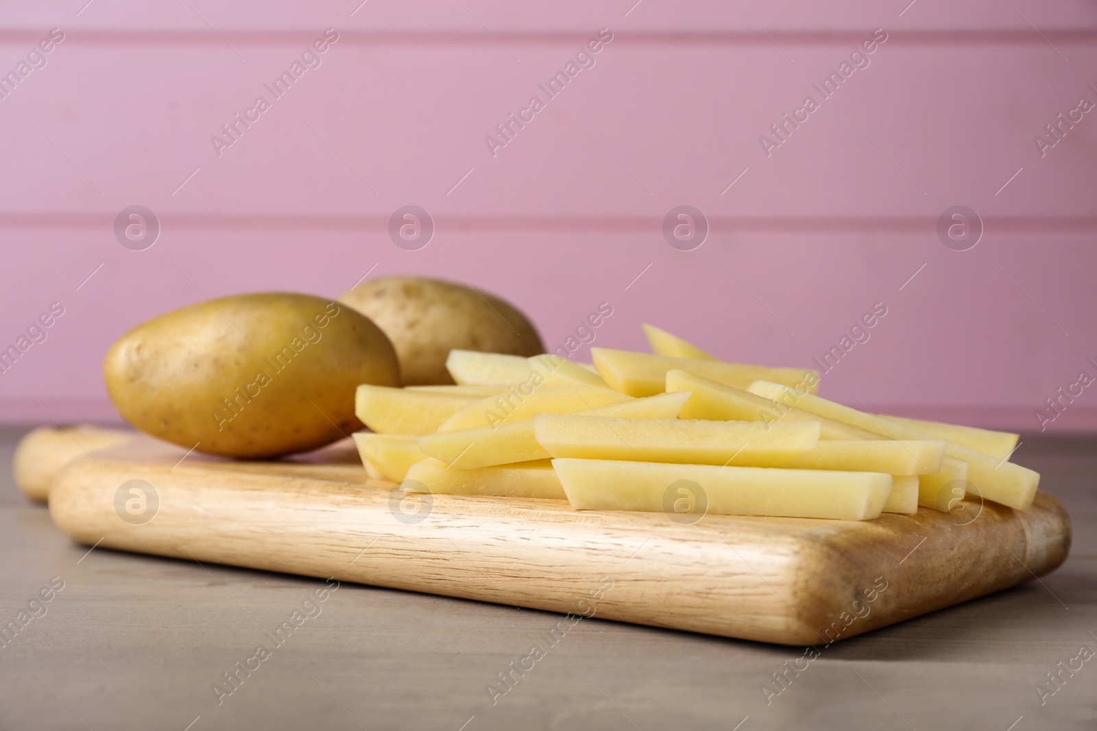 Photo of Whole and cut raw potatoes on wooden board, closeup