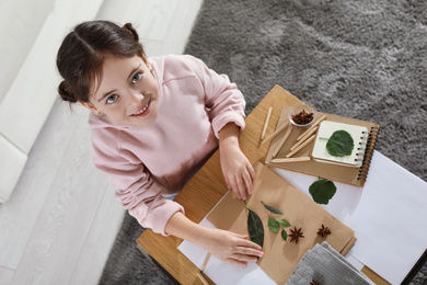 Photo of Little girl working with natural materials at table indoors, top view. Creative hobby