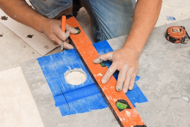 Worker making holes for bathroom water pipes in tile indoors, closeup