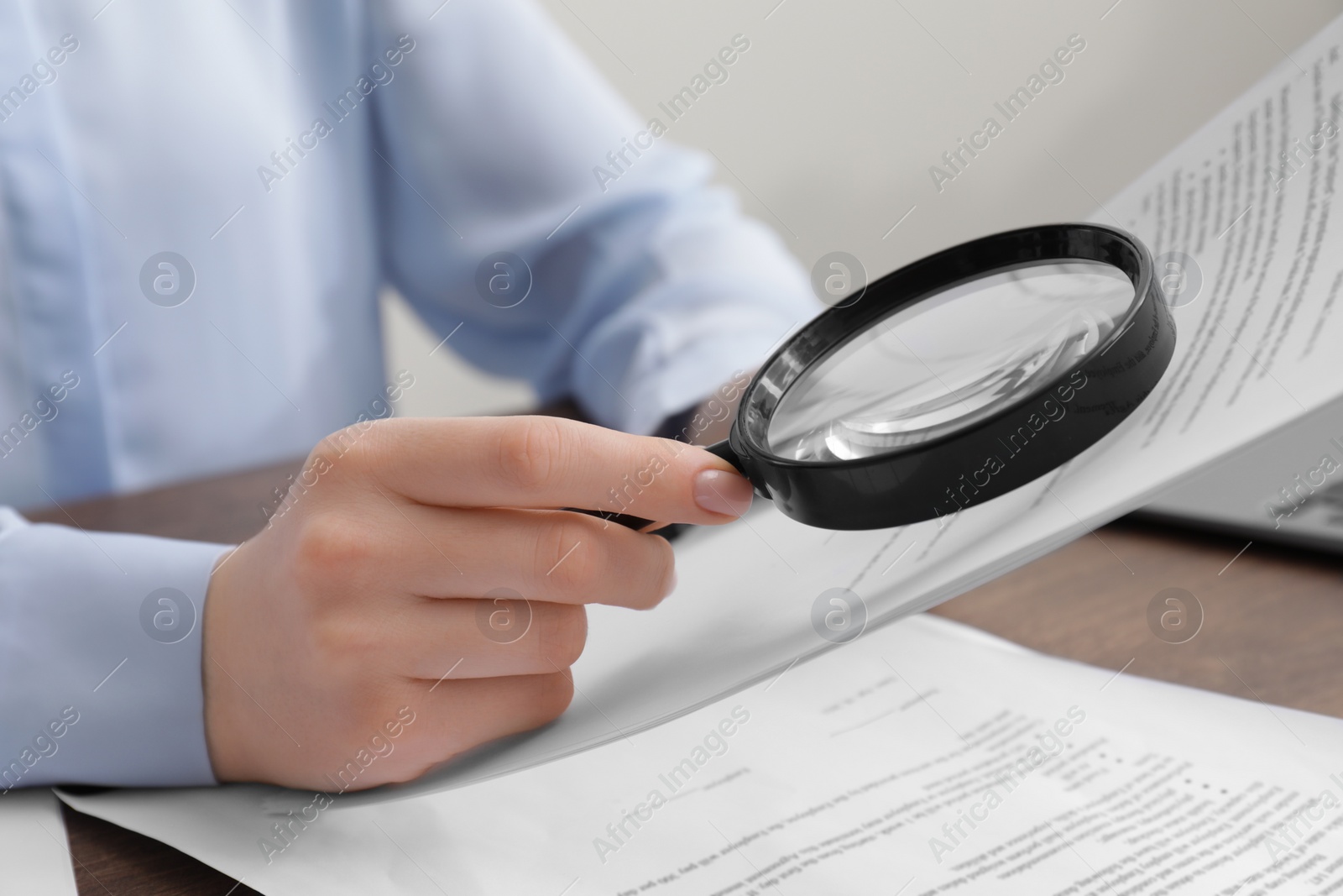 Photo of Woman looking at document through magnifier at table indoors, closeup. Searching concept