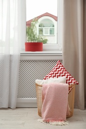 Basket with pillows and plaid near window in modern room