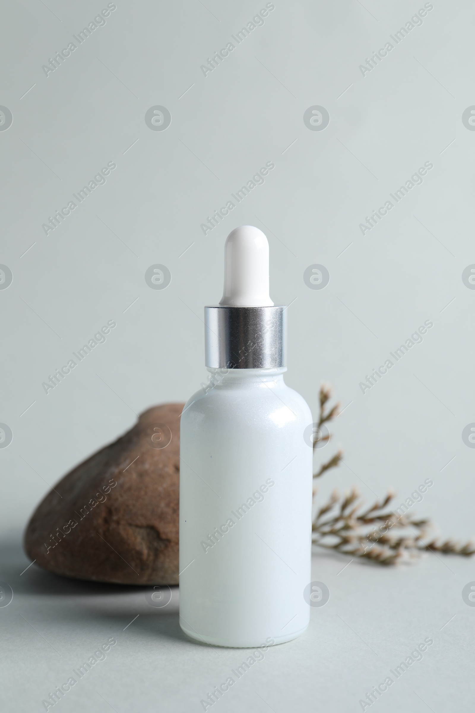 Photo of Bottle with cosmetic serum, stone and dry flowers on light grey background