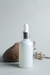 Bottle with cosmetic serum, stone and dry flowers on light grey background