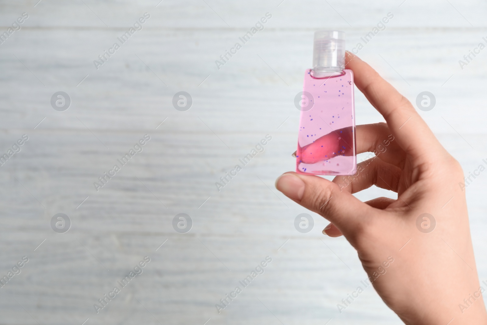 Photo of Woman holding antiseptic gel on light background, closeup. Space for text