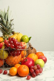 Photo of Metal basket with different fresh fruits on white marble table