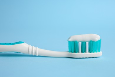 Brush with toothpaste on light blue background, closeup
