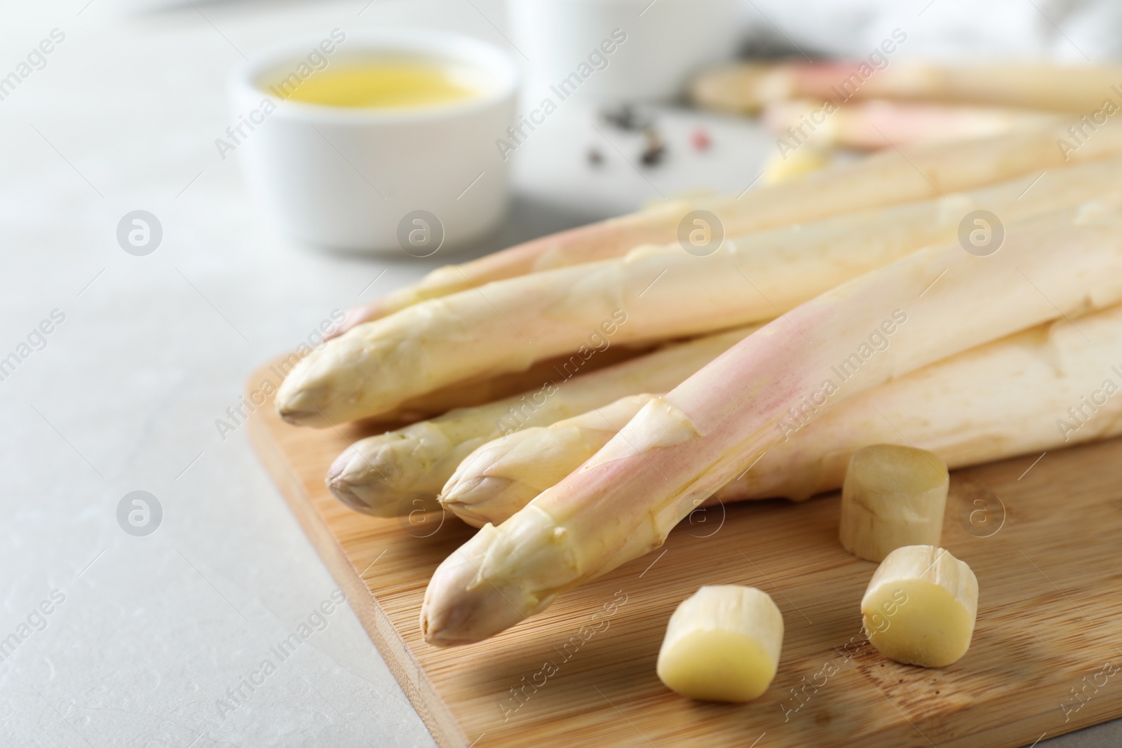 Photo of Fresh white asparagus and wooden board on grey marble table, closeup