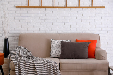 Photo of Soft pillows on sofa near white brick wall
