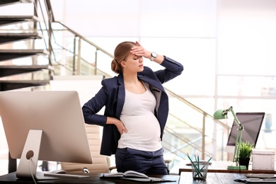 Photo of Young pregnant woman suffering from pain while working in office