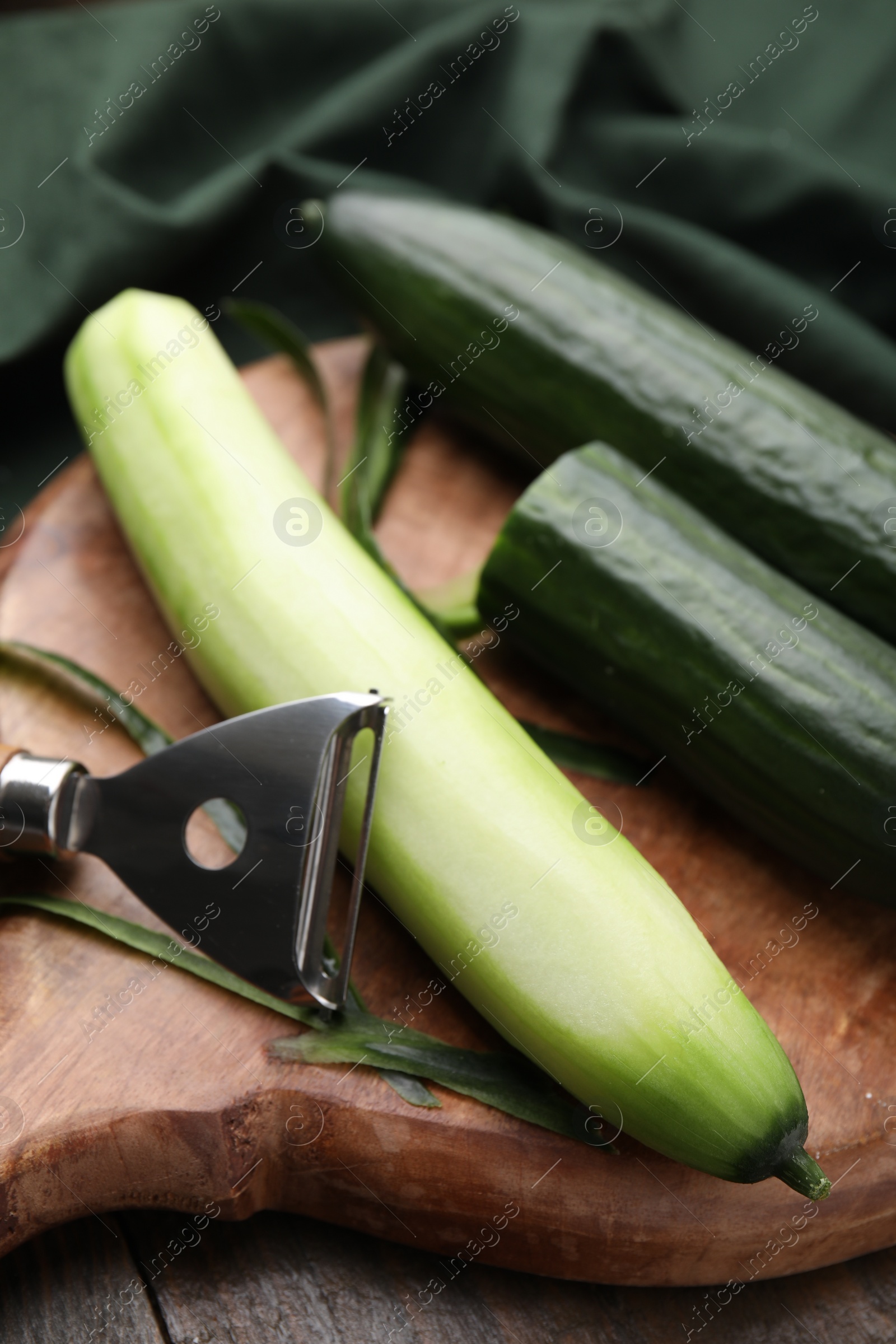 Photo of Fresh cucumbers and peeler on wooden table, closeup