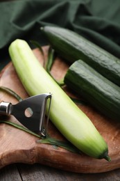 Fresh cucumbers and peeler on wooden table, closeup