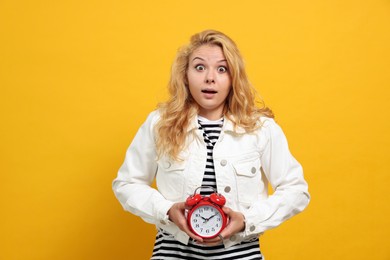 Photo of Emotional woman with alarm clock in turmoil over being late on yellow background