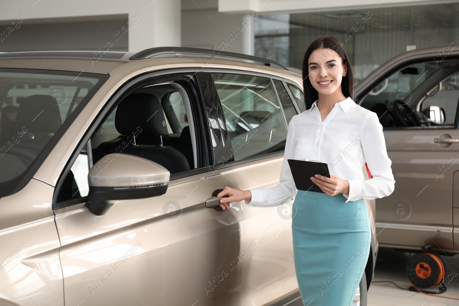 Photo of Saleswoman with clipboard near car in dealership