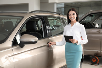 Photo of Saleswoman with clipboard near car in dealership