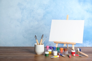 Photo of Wooden easel with blank canvas board and painting tools for children on table near color wall. Space for text