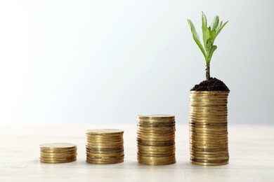 Photo of Stacks of coins with green seedling on white wooden table, space for text. Investment concept