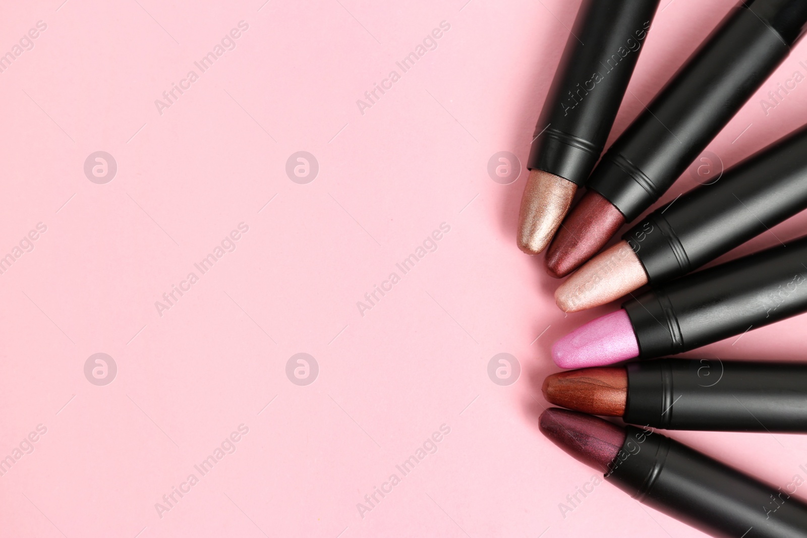 Photo of Set of bright lipsticks in black tubes on pink background, flat lay. Space for text