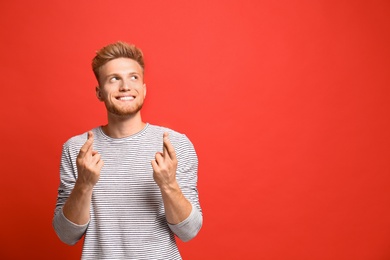 Portrait of hopeful man with crossed fingers on red background, space for text