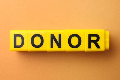 Word Donor made of yellow cubes on orange background, flat lay