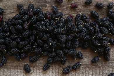 Heap of delicious ripe black mulberries on wooden table, flat lay
