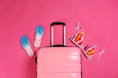 Photo of Stylish suitcase, bikini top and flip flops on color background, top view