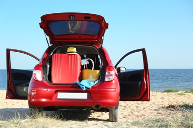 Photo of Suitcase and beach accessories in car trunk on sand near sea. Space for text