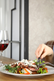 Photo of Woman eating delicious salad with roasted meat at wooden table, closeup. Space for text