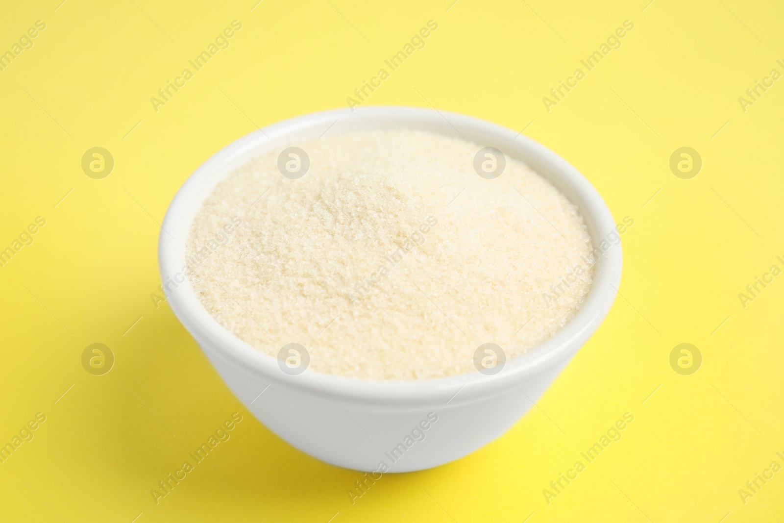 Photo of Gelatin powder in bowl on yellow background, closeup