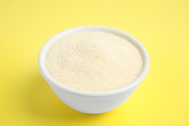 Photo of Gelatin powder in bowl on yellow background, closeup