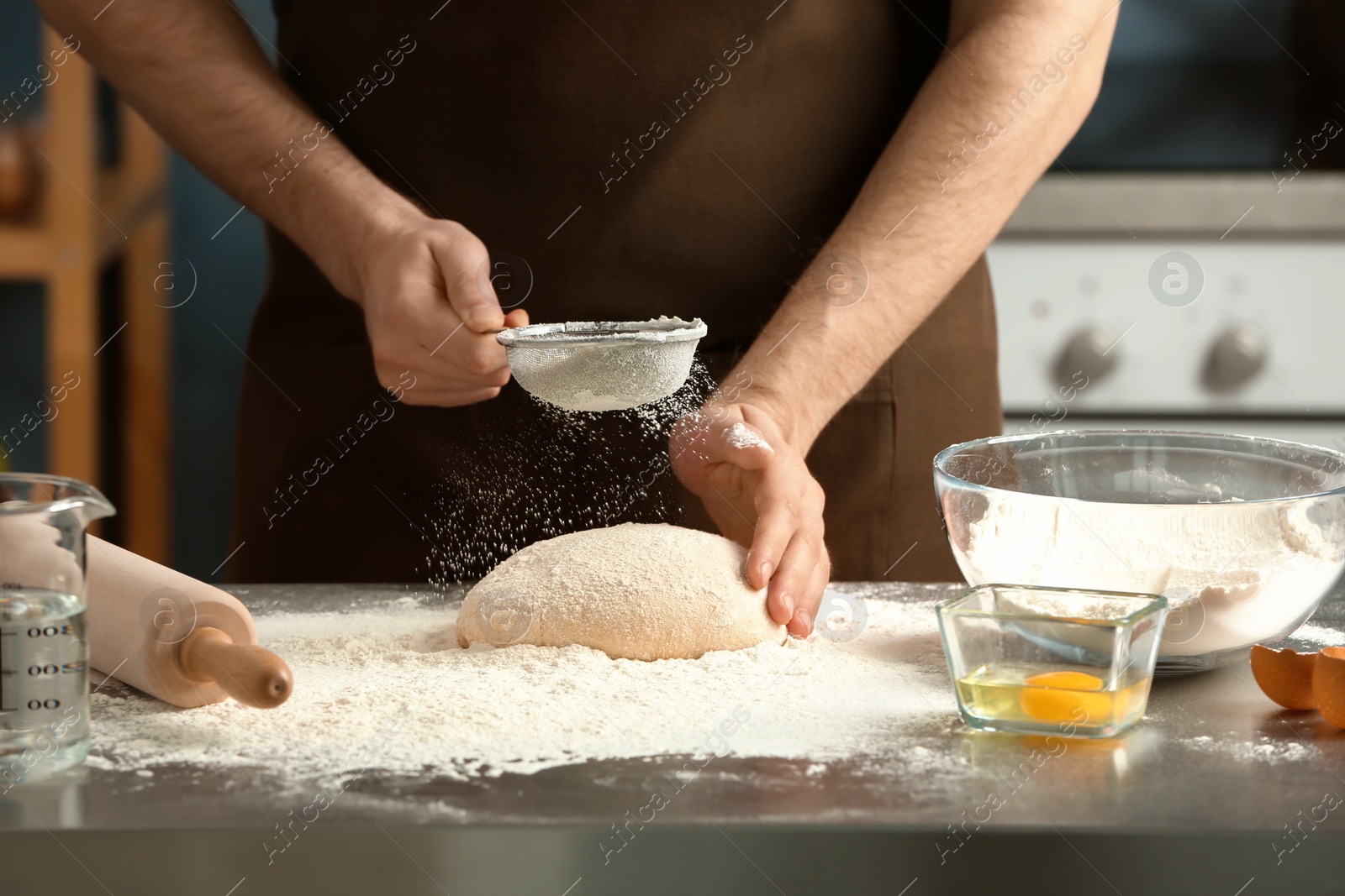 Photo of Man sprinkling flour over dough on table in kitchen