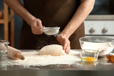 Photo of Man sprinkling flour over dough on table in kitchen