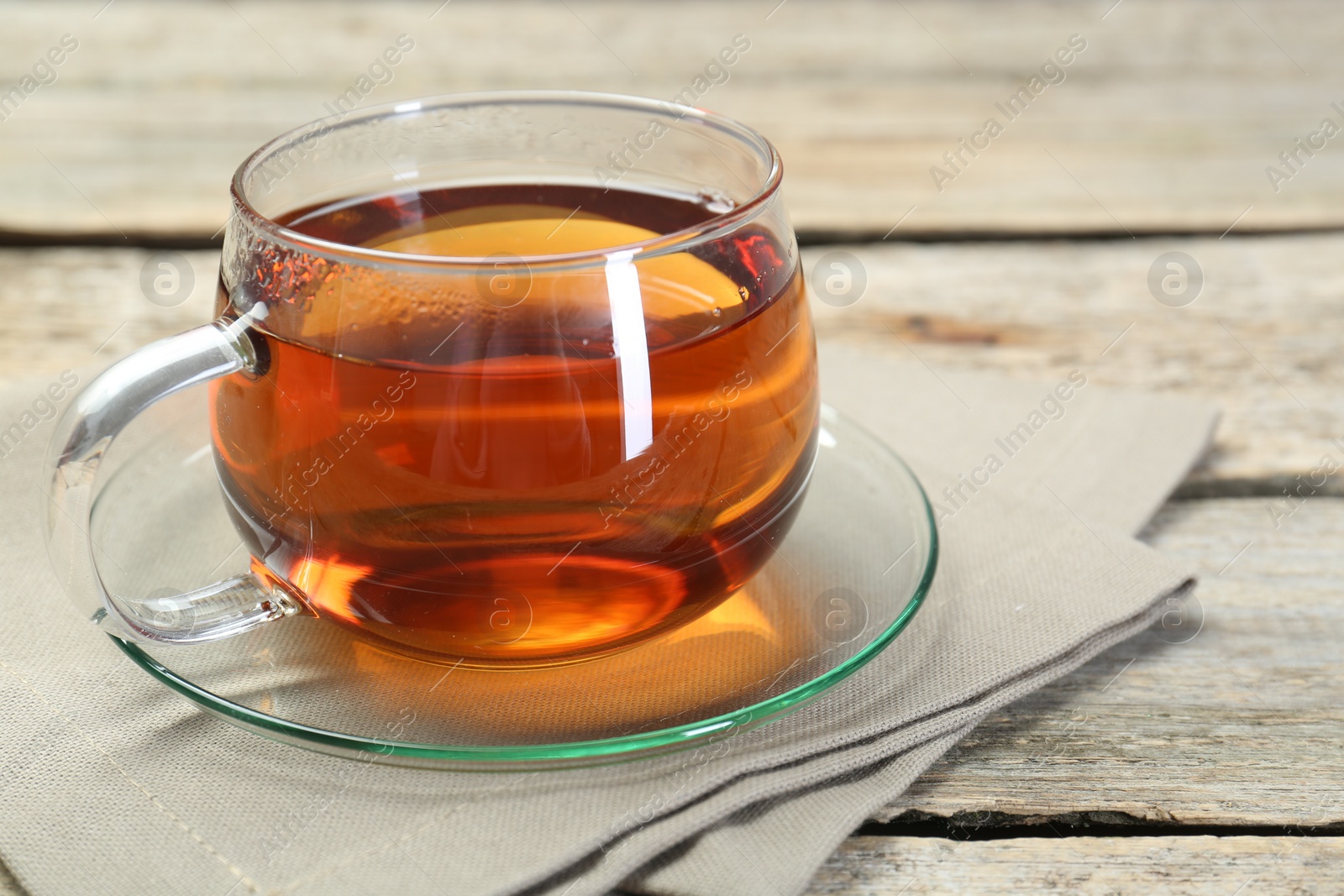 Photo of Aromatic tea in glass cup and napkin on wooden table