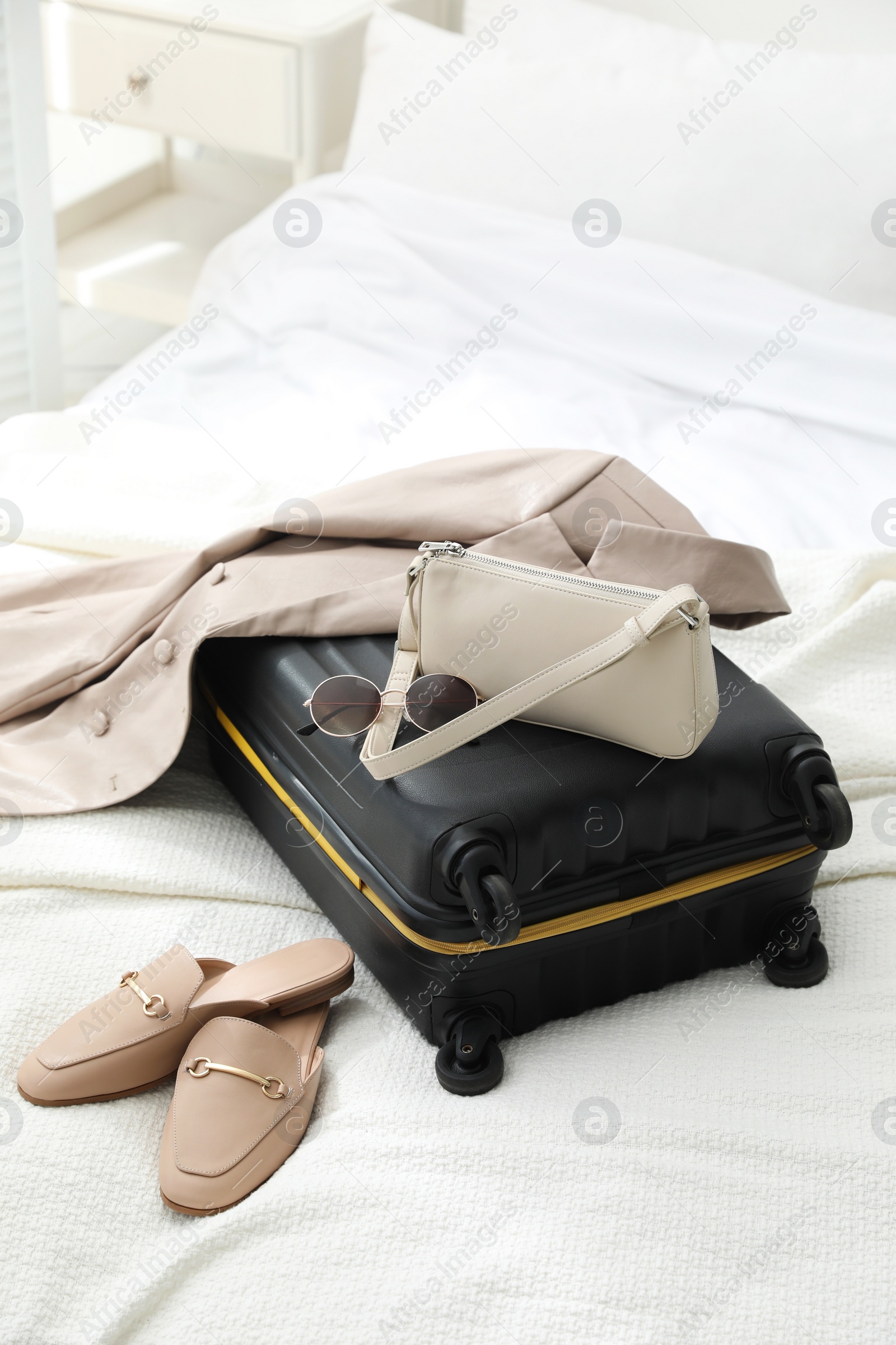 Photo of Suitcase packed for trip, shoes, jacket and fashionable accessories on bed