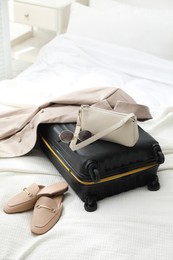 Suitcase packed for trip, shoes, jacket and fashionable accessories on bed