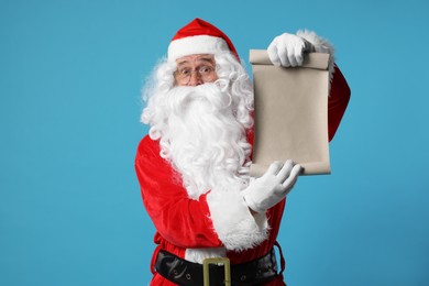 Photo of Merry Christmas. Santa Claus showing blank paper sheet on light blue background, space for text